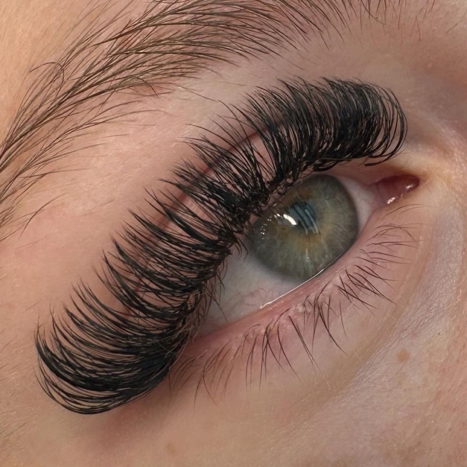 Fluffige Volumen-Wimpernverlängerung an einem grünen Auge